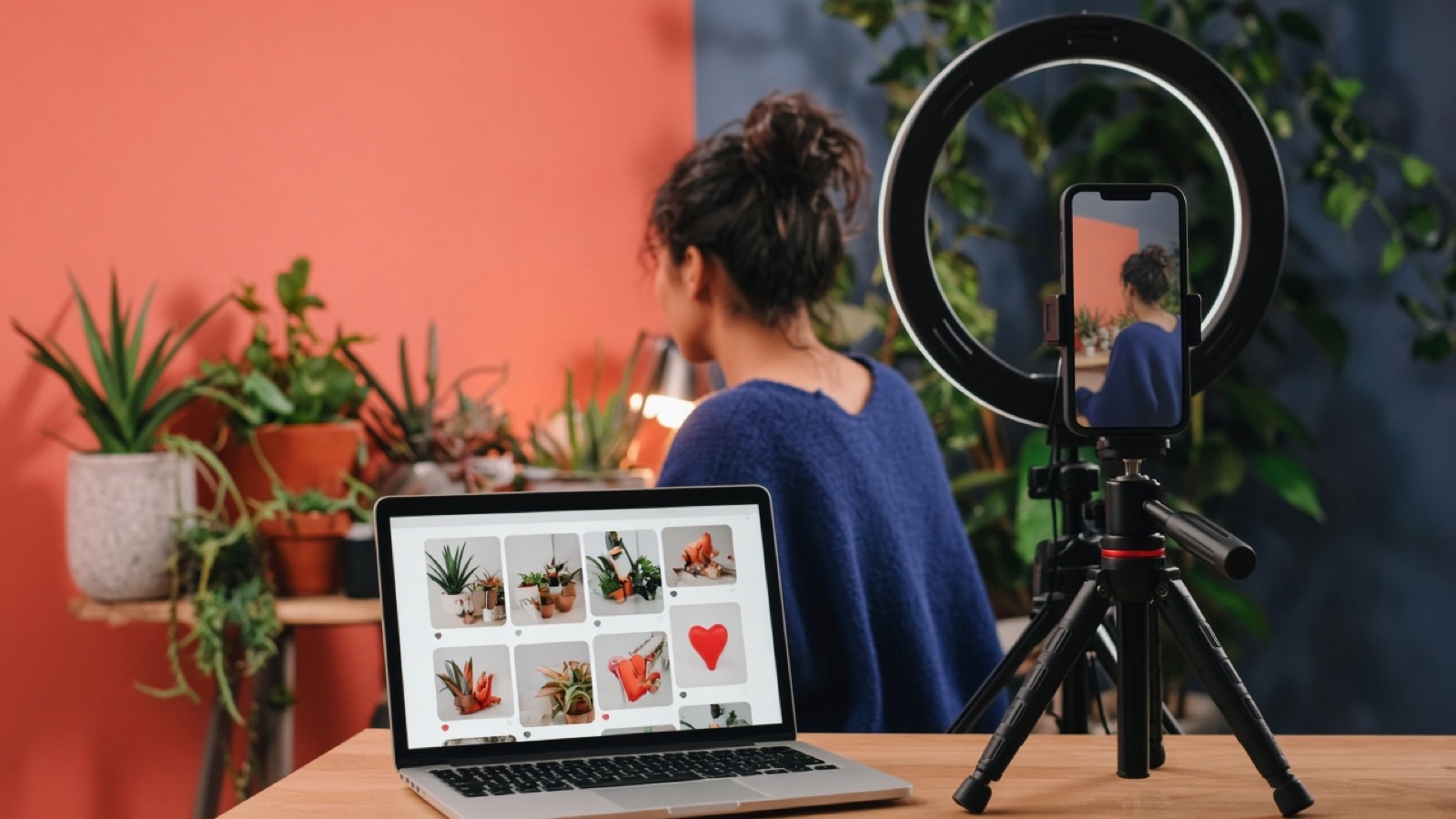 Content studio where a creator films a vertical phone video beside a laptop showing a photo feed